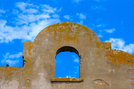 Old Spanish mission wall and window arch under blue sky with scattered cloudsの写真素材