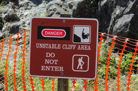 Warning sign with orange fencing ensures safety in rocky cliff area.の写真素材