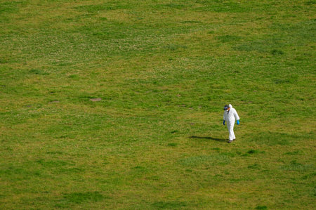 Lone figure in protective gear walking in a vast green field under a clear skyの写真素材