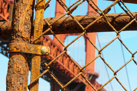 Rusty fence framing an iconic red bridge against a bright blue sky.の写真素材
