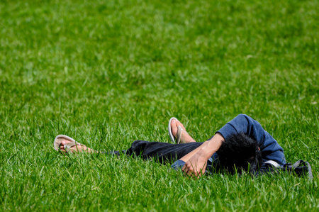 A person relaxes on lush green grass, wearing casual clothes on a sunny day.の写真素材