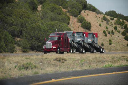 Red truck hauls new semi-trucks on highway through scenic landscapeの写真素材