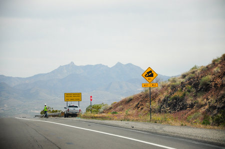 Scenic mountain road with vehicle and steep incline warning on cloudy day