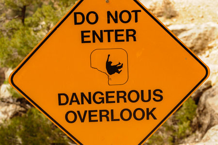 Yellow warning sign cautions visitors about dangerous national park overlookの写真素材