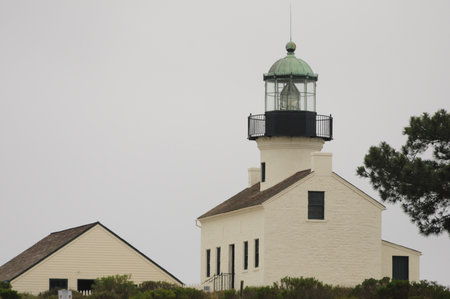 Historic lighthouse in San Diego, surrounded by greenery under a cloudy sky.の写真素材