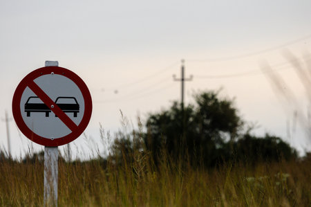 Rural prohibition sign by grassy field with trees and power lines at dawnの写真素材