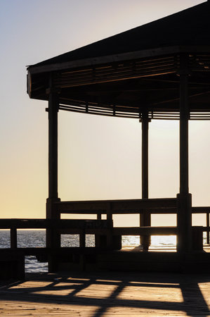 Silhouetted gazebo overlooking tranquil ocean at sunset, shadows on deckの写真素材