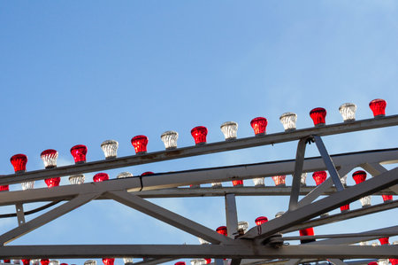 Red and clear bulbs adorn metal framework under blue sky, creating festive moodの写真素材