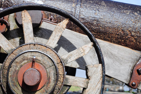 Close-up of a rustic cannon wheel showcasing weathered wood and iron details.の写真素材