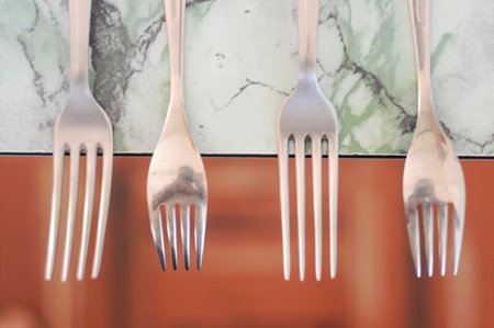 Four stainless steel forks on marble with subtle reflections under soft lighting