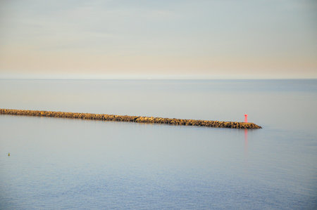 Lighthouse on calm sea breakwater under pastel skyの写真素材