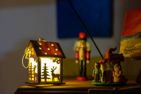 Details of the Christmas decoration with a small cabin illuminated from the inside and other Christmas characters next to it. The figure of a nutcracker can be seen out of focus in the backgroundの写真素材