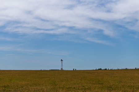 Expansive rural landscape with a solitary windmill under a vast blue sky.の写真素材