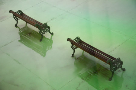 Ornate benches on vibrant green surface in serene, symmetrical settingの写真素材