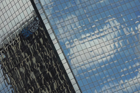 Skyscraper reflecting sky and clouds in glass facade, abstract urban sceneの写真素材