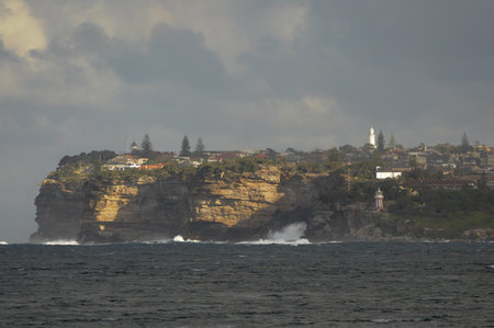 Coastal landscape with waves and cliffside homes near lighthouse at duskの写真素材