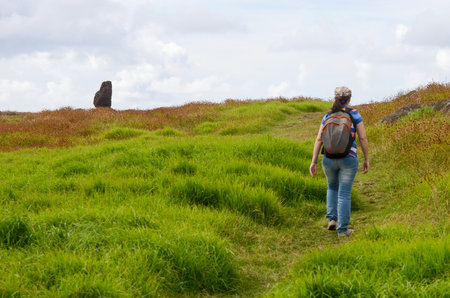 Woman hiking towards statue in lush grass under cloudy skyの写真素材