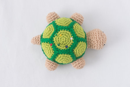 Crocheted turtle pincushion with pins on white background
