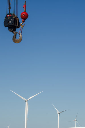 Crane hook over wind turbines, symbolizing renewable energy progressの写真素材