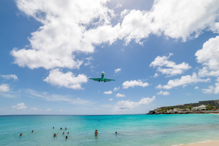 An airplane flies low over a vibrant tropical beach with people swim. Sunny, exciting, and adventure travelのeditorial素材