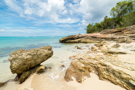 Idyllic Caribbean beach scene with turquoise waters, rugged rocks, golden sand, and lush green...