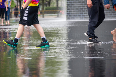 Close-up view of people walking through shallow water at a public art installation in an urban park. Playful, casual