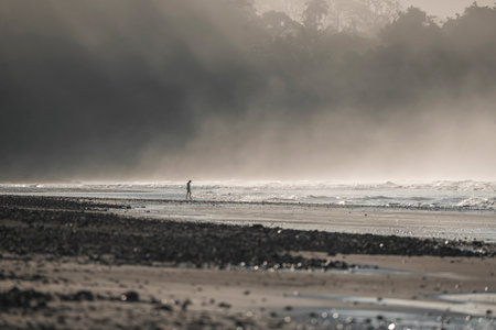 Silhouette of a man walking on the beach with fog in the backgroundの写真素材