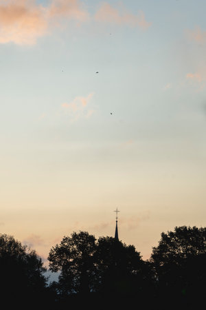 Silhouette of a church at sunset with a bird flying in the skyの写真素材