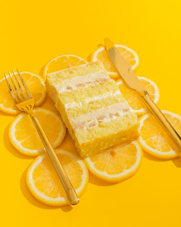 Lemon cake on yellow background with cutlery and slice of orangeの写真素材