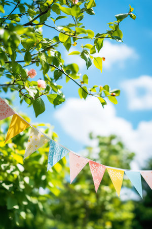 Colorful pennant string decoration in green tree foliage against blue sky; summer party background with space for textの素材