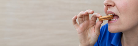 A close up side view of a woman in a blue shirt eating a biscuit, concept related to snacking or...