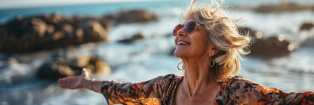Joyful mature woman with sunglasses embracing freedom on a sunny beach holidayの素材