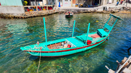 Brightly painted traditional wooden fishing boat moored in clear tropical waters near a coastal villageの写真素材