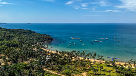 A serene tropical coastline dotted with palm trees, boats floating in the azure sea with clear skies above, ideal for vacation conceptsの写真素材