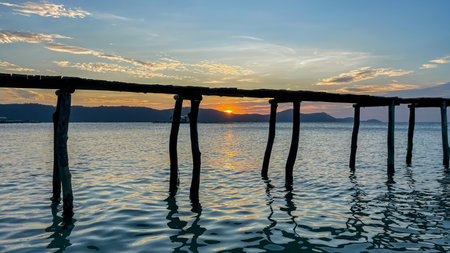 Tranquil seascape with wooden pier silhouette against a stunning sunset background, reflecting on calm ocean watersの写真素材
