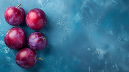 Five fresh plums on a textured blue background, suitable for healthy eating or culinary conceptsの素材