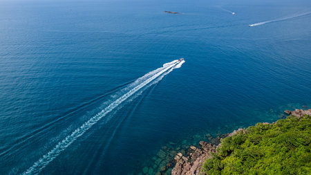 Aerial view of a speedboat cruising through blue sea waters near a tropical coast, creating a white...