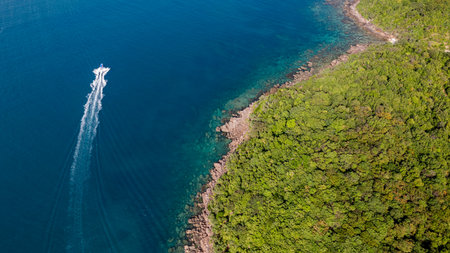 Aerial view of a speedboat creating a white wake near a lush green coastline, showcasing the concept...