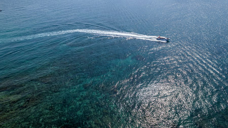 Aerial view of a speedboat cruising on a clear blue sea, leaving a white wake behind