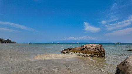 Tranquil tropical beach scene with clear water, rocks in the foreground, and boats on the horizon, ideal for summer vacation conceptの写真素材