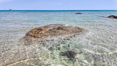 Clear tropical waters with visible rocks and a solitary boat on the horizon, depicting serene beach...