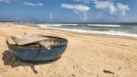 Traditional round Vietnamese fishing boat on a tranquil sandy beach with ocean waves and ample copy space in the sky, evoking a sense of peaceful seaside lifeの写真素材