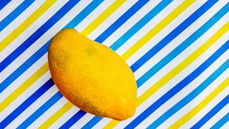 Fresh ripe mango on a vibrant blue and white striped background with copy space, suitable for food...