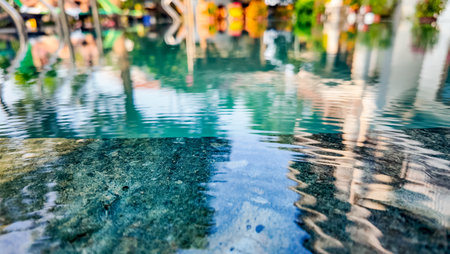 Tranquil water surface with blurred reflection of people enjoying a tropical resort pool, ideal for...