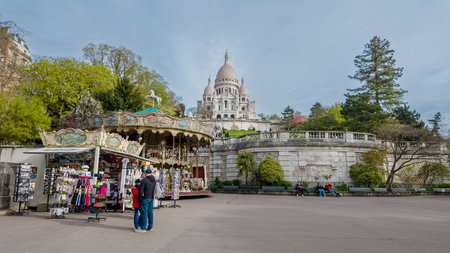 Bright spring day at Montmartre with tourists near souvenir stalls and a vintage carousel, Sacre Cur Basilica in the backdrop, Paris, France, April 14th, 2024のeditorial素材