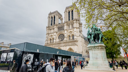 Tourists exploring the iconic Notre Dame Cathedral and Charlemagne statue on a cloudy day in Paris,...