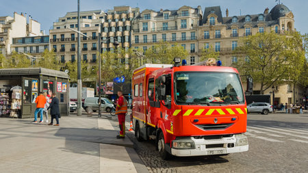 French firefighter in action beside a bright red engine on a bustling Paris street, illustrating...