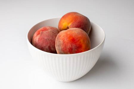 A white bowl filled with fresh, ripe peaches symbolizing summer harvest and nutritious eating on a white backgroundの写真素材