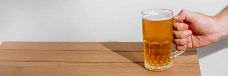 A beer enthusiasts hand holding a frosty mug of golden beer on a wooden table, perfect for Oktoberfest celebrationの写真素材