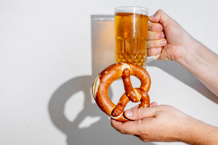 Person holding a pretzel and a beer mug, celebrating Oktoberfest with traditional German snacks and drinksの写真素材